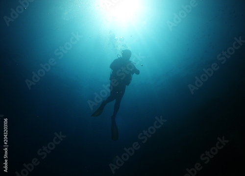 Canvas Print Scuba diver silhouette ascending toward dramatic sunburst in deep blue ocean