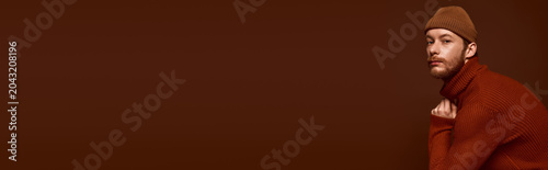 Canvastavla Handsome red haired man poses stylishly in cozy autumn fashion against a warm brown backdrop