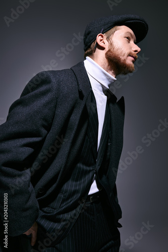 Stylish red haired man in fashionable attire poses confidently against a moody backdrop.