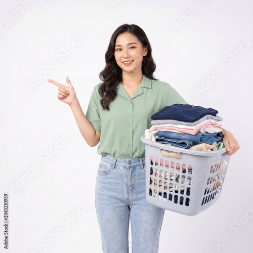 Young Asian Woman Carrying Laundry Basket Full of Clothes and Pointing to Copy Space