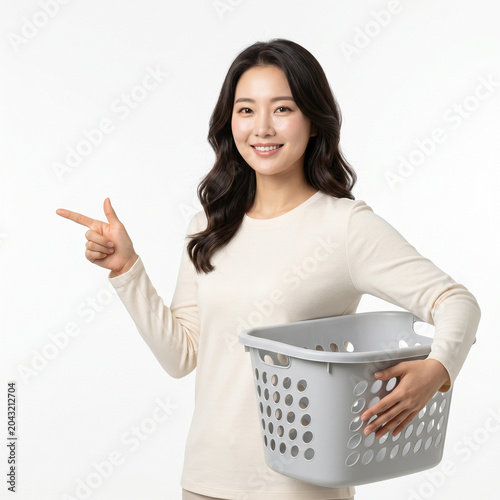 Smiling Asian Woman Holding Empty Laundry Basket and Pointing to Copy Space on White Background