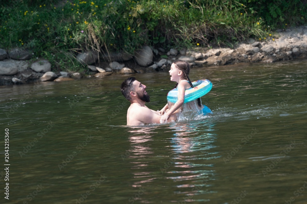 Fototapeta premium A father and daughter enjoy a playful moment in a river, the girl using an inflatable ring.