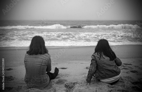 Two young people from behind, sitting in front of the sea on a winter day
