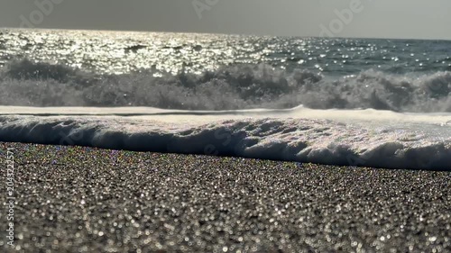 Ocean waves glistening under sunlight on sandy beach background