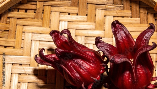 Displaying two deep red roselle calyces on woven bamboo tray showing curved rim and warm shadows