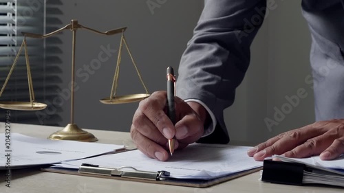 Male legal consultant signing contract papers with justice scale in office, showing law firm service, client agreement, risk control, business protection, and trusted legal advice.