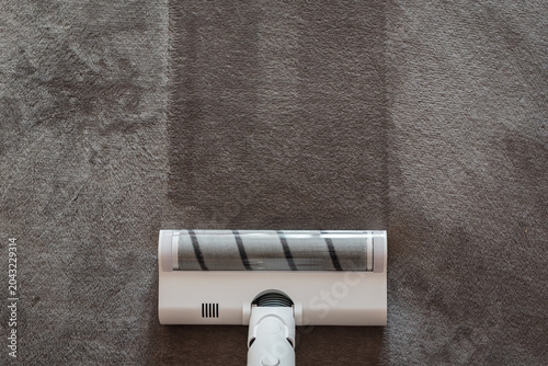 Foto Top view of a powerful white cordless vacuum cleaner on a soft grey carpet, motorized floor brush leaving a distinct clean track, efficient deep cleaning and spotless home hygiene result