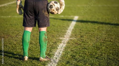 Goalkeeper standing on a grassy field holding a soccer ball, ready for the game to begin