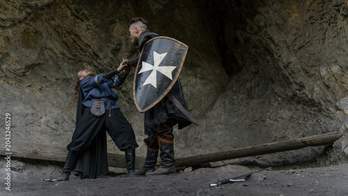 Bild auf Leinwand A knight with a shield defends against an attacker in a rocky, medieval setting