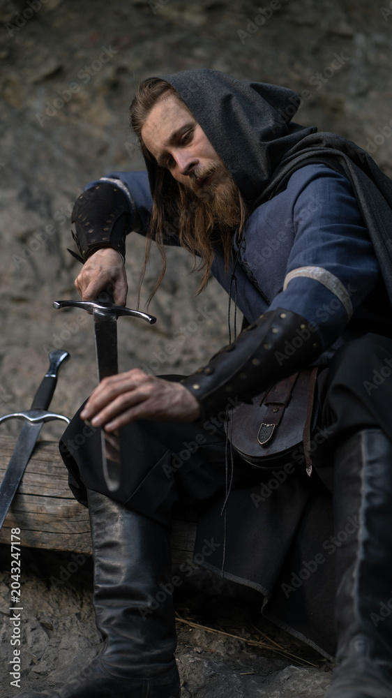 Fototapeta premium Weary warrior rests, hand on sword hilt amidst weathered stone.