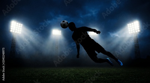 Dynamic silhouette of a soccer player leaping to head the ball against the powerful glow of stadium floodlights, capturing the intensity of professional sports action