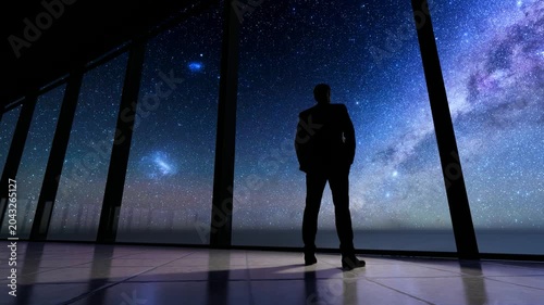 A businessman's silhouette as he stands at the window of an office building, gazing up at the starry sky