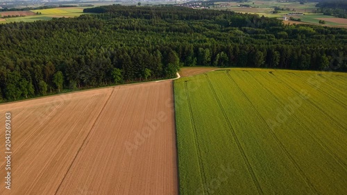 Aerial drone inspection of German farmland in late May showing green crops and a harvested brown field divided by narrow strip, highlighting seasonal growth contrast and rural agriculture in Germany