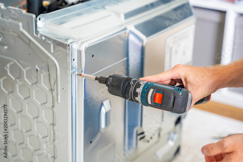 Technician removing rear cover of electric oven before diagnostics and repair. Accessing internal components concept