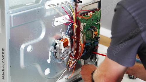 Technician replacing electronic control board inside disassembled electric oven during repair. Appliance maintenance and professional service concept