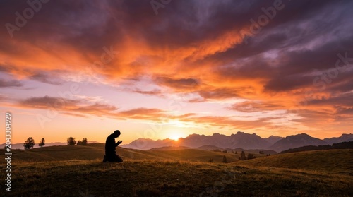 Man kneeling in prayer at sunrise over mountains, dramatic sky