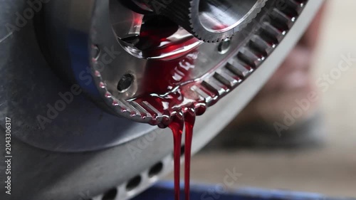 ​Close-up of bright red hydraulic oil or transmission fluid leaking and dripping down from a metal splined shaft component.