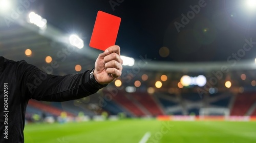 Football referee holding red card during night match under stadium lights