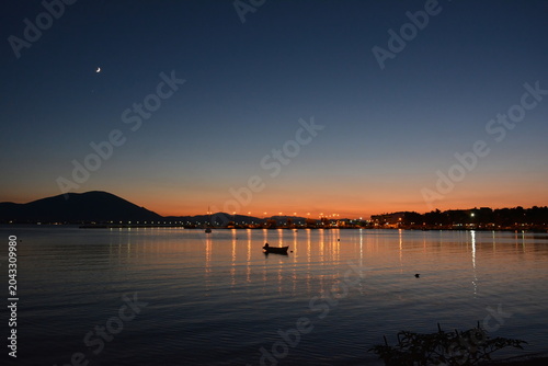 Sunset colors in the sky and reflected on the sea, with the moon and town lights at a distance. Euboea (Evia), Greece