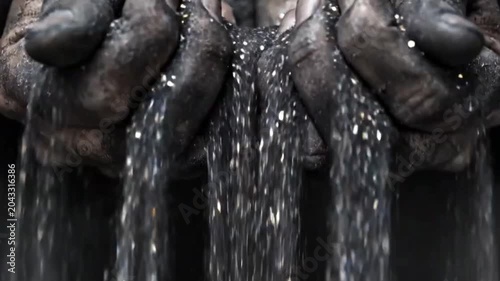 Dirty, ash-covered hands holding sparkling silver glitter, contrast between grime and luxury or precious materials, macro shot.