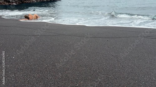 Woman relaxing on black sand beach with copy space, Bali

