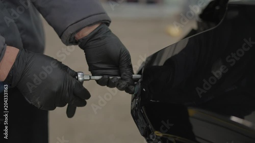He carefully detaches a car part.This process happens in a workshop.The closeup focus shows manual labor.The man uses a hand tool