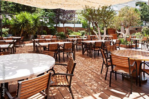Fotografie Empty outdoor restaurant terrace with wooden tables chairs and dappled sunlight
