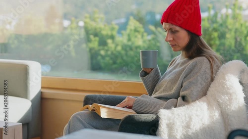 A woman reading by a large window and enjoying scenic snowy mountain view.