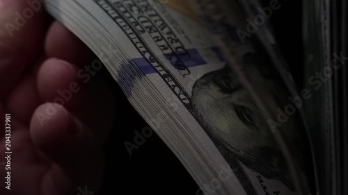Close-up of hand flipping through stack of U.S. hundred dollar bills in slow-motion