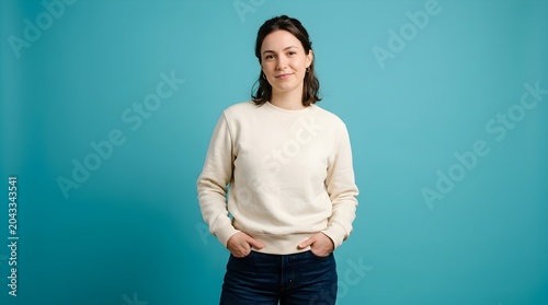 Portrait of a young woman wearing a beige sweatshirt standing against a solid turquoise background