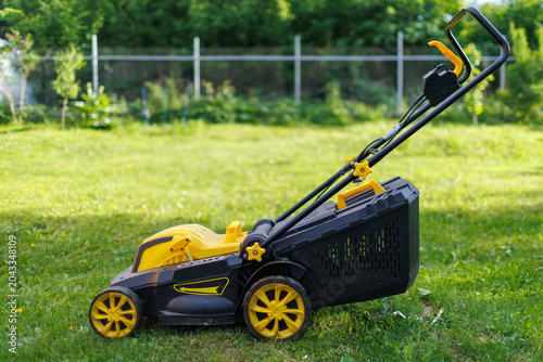 Side profile view of a yellow wheeled lawn mower apparatus standing on a green grass field