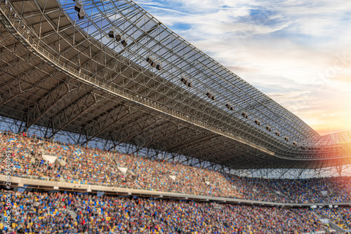 Foto A large crowd of people fills the stands of a modern sports stadium under a massive steel roof structure at sunset