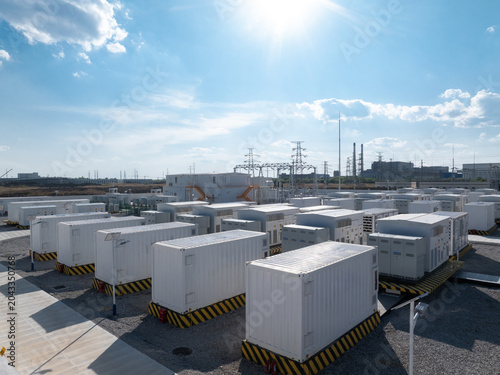 White containerized energy storage systems arranged in an outdoor power station facility