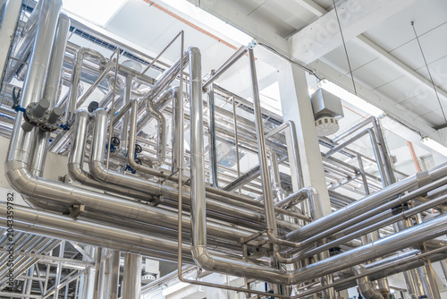 Modern industrial factory interior with stainless steel pipes and processing machinery. Clean automated production line in food, dairy, or chemical plant engineering industry.