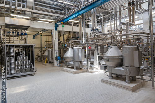 Modern industrial factory interior with stainless steel pipes and processing machinery. Clean automated production line in food, dairy, or chemical plant engineering industry.