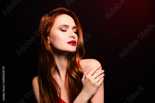 Elegant young woman with red hair and glamorous makeup in stylish pose on dark background