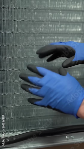 HVAC technician cleaning air conditioner condenser coils with gloves.