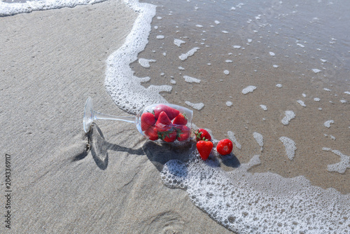 strawberries spilled from a glass on a sandy beach, surrounded by waves