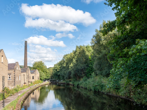The Rochdale canal in Hebden Bridge with houses and trees reflected in the water in summer sunlight