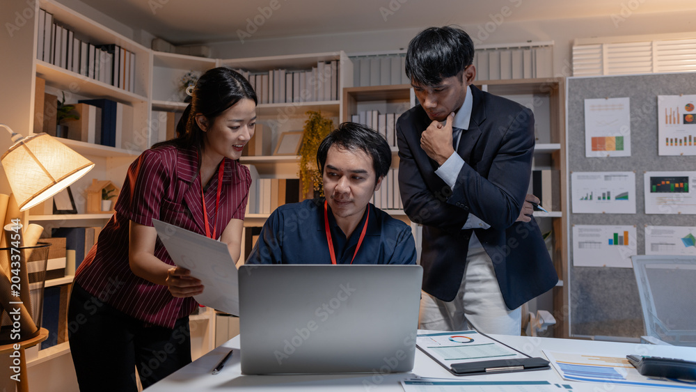 Fototapeta premium Business team discussing work together in office, analyzing reports and data on laptop and documents, showing collaboration, planning, and problem solving during a productive meeting.