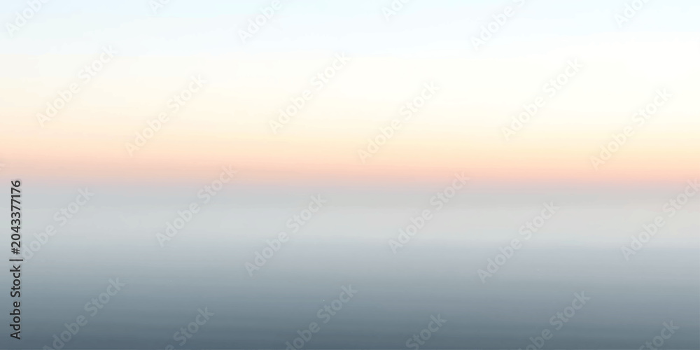 Fototapeta premium A tranquil seascape at dusk, where the sky fades from pale orange to soft pink, meeting the calm, muted blue of the water.