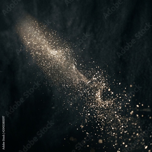 Golden sparkling dust particles illuminated on a dark textured background.
