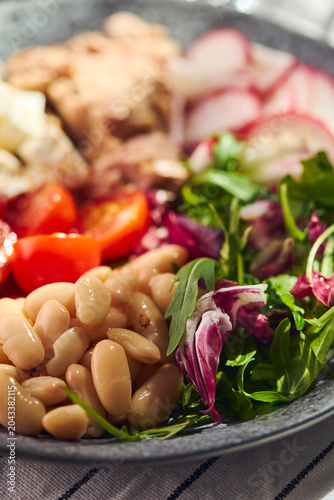 Healthy Mediterranean salad with canned tuna, white beans, feta cheese, cherry tomatoes, and greens on a stone plate.