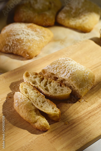 Close-up of sliced homemade ciabatta bread with flour dusting, revealing airy porous crumb texture on a rustic wooden cutting board.