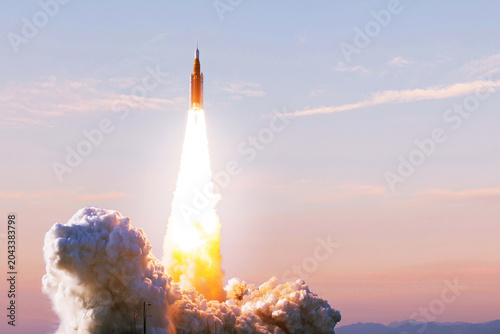 space rocket launches into the sky at sunrise, leaving thick clouds of smoke and a bright trail of fire behind as it begins its mission. Spaceship lift off to the space Start