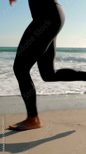 Athletic woman jogging along the beach. Vertical video.
