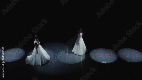 Cinematic wide shot of two elegant models in white wedding gowns posing on dark runway with large circular LED spotlight rings at bridal fashion show. Perfect for wedding, fashion, and luxury content.