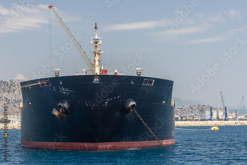 An oil tanker in an industrial port. Transportation of petroleum products by sea. An industrial vessel. A crane is installed on the deck of the vessel. Cranes for loading ships are visible in the port