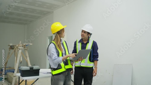 Indoor construction site hard hat safety vest worker planner laptop inspection renovation project management teamwork with two person planning and consultation in office room white area