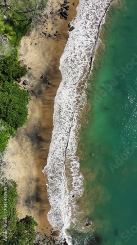 Aerial view of a tropical beach with waves and rocks beside rainforest